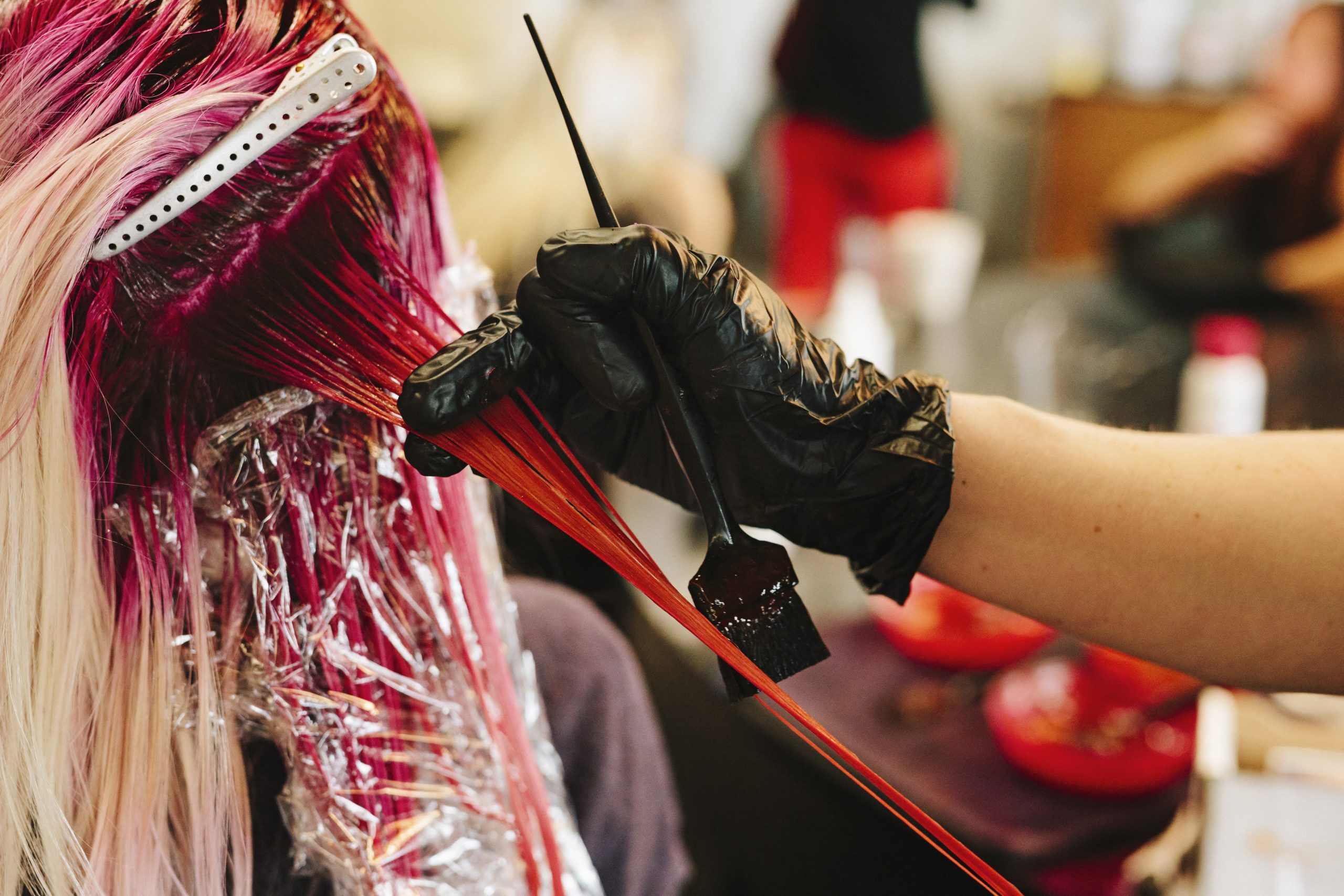 顧客のブロンドのロングヘアにピンクのヘアカラーを施すヘアカラーリスト